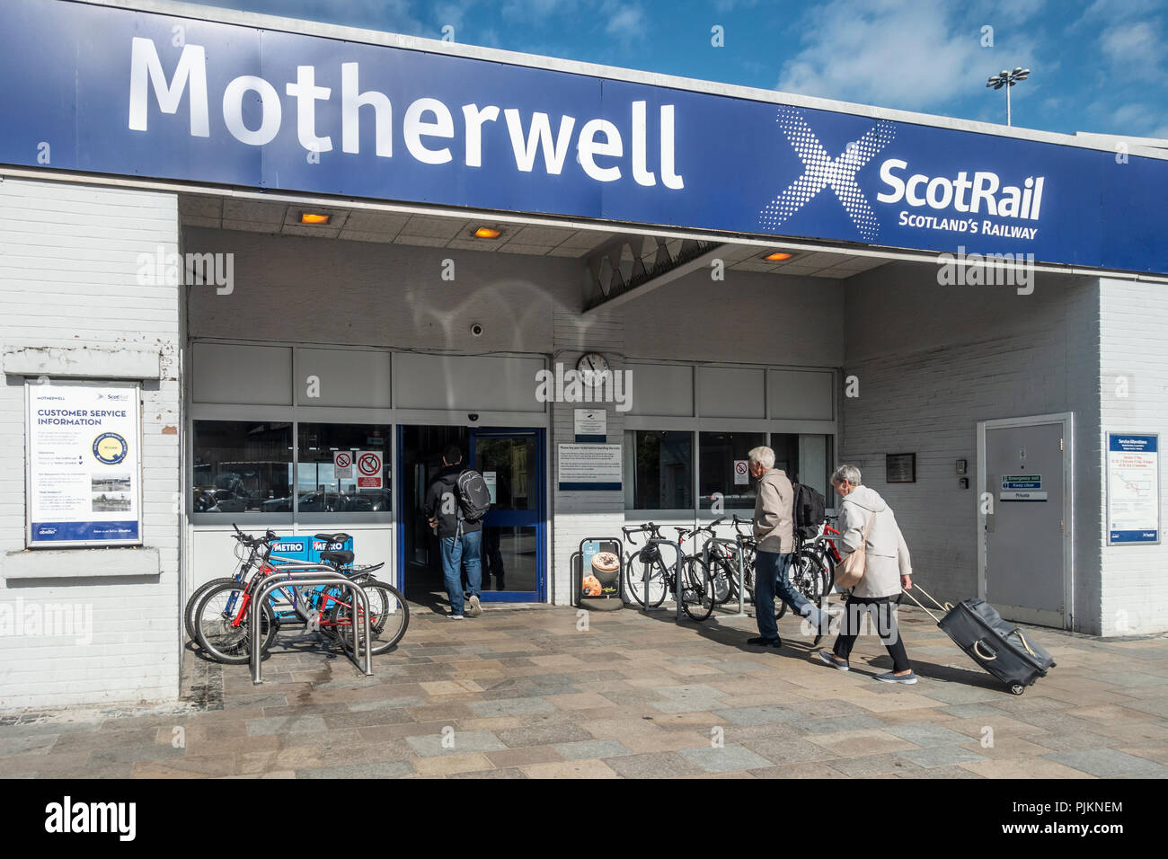 I passeggeri che provengono Motherwell ScotRail stazione ferroviaria. Due uomini con zaini, una donna tirando una valigia su ruote. Rastrelliere per biciclette. Nord Lanarksh Foto Stock