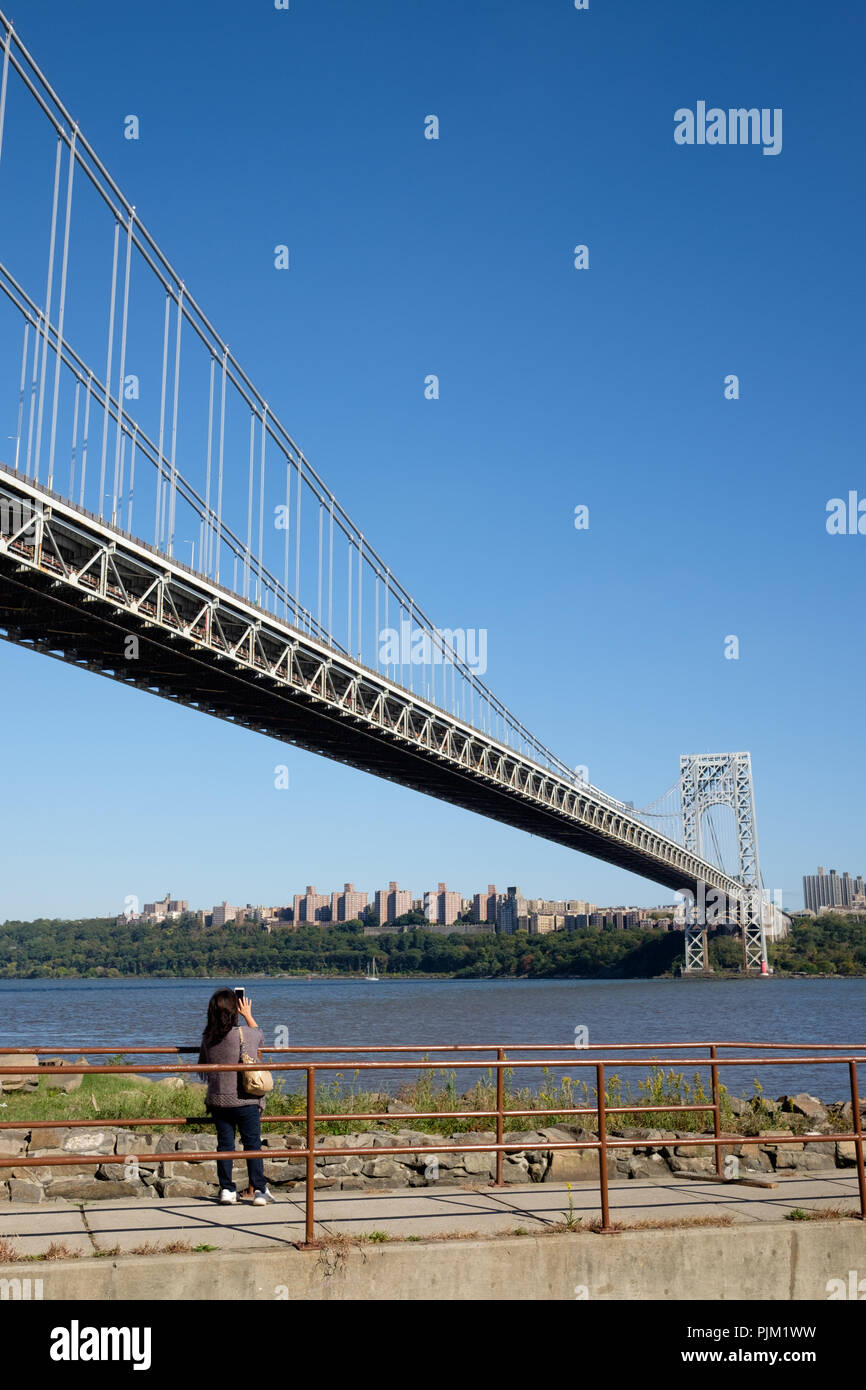 Un turista scatta una fotografia del George Washington Bridge da Fort Lee, NJ con il fiume Hudson, faro rosso piccolo e la città di New York. Foto Stock