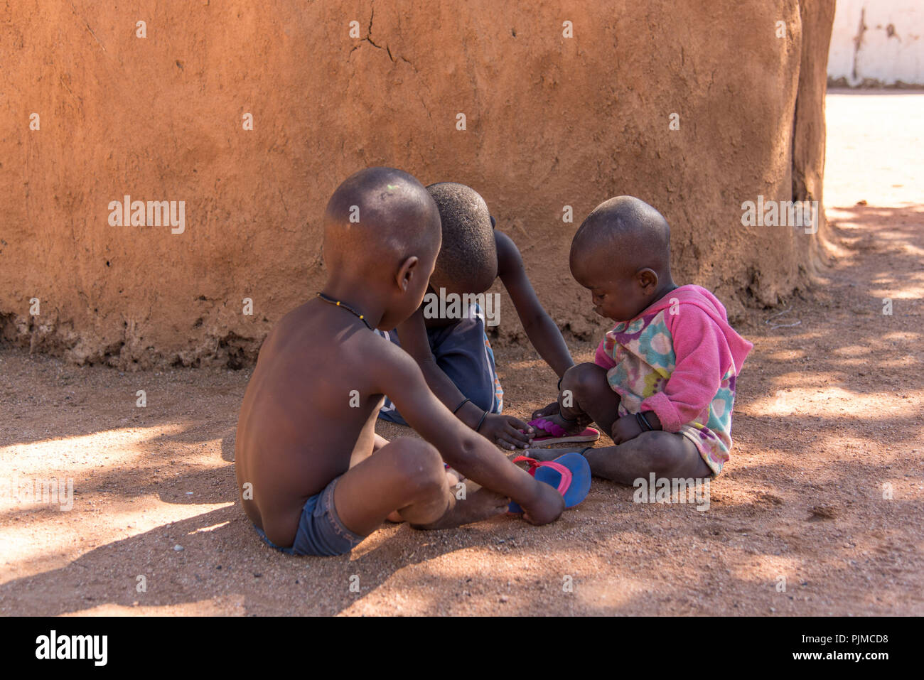 Tre Himba bambini giocano nell'ombra di una capanna di fango Foto Stock
