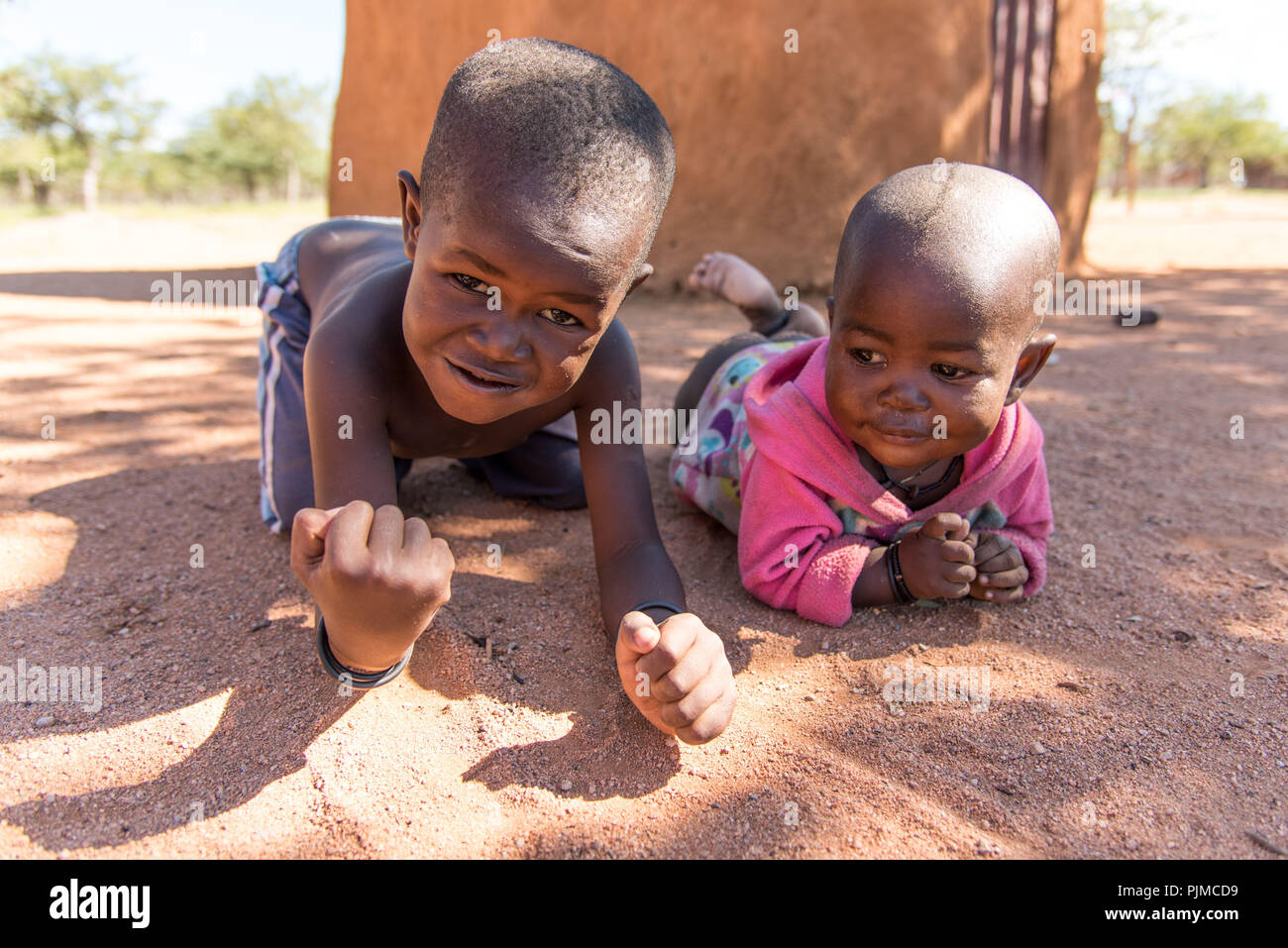 Due Himba bambini giocano nell'ombra di una capanna di fango, guardando nella telecamera Foto Stock