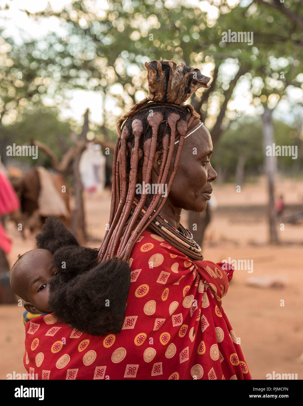 Himba bambino viene portato da sua madre sulla sua schiena, guardando la telecamera Foto Stock