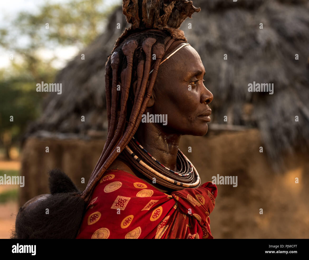 Ritratto di una donna Himba nell'ultima luce del sole, profilo laterale. Il bambino sulla schiena è solo visibile Foto Stock