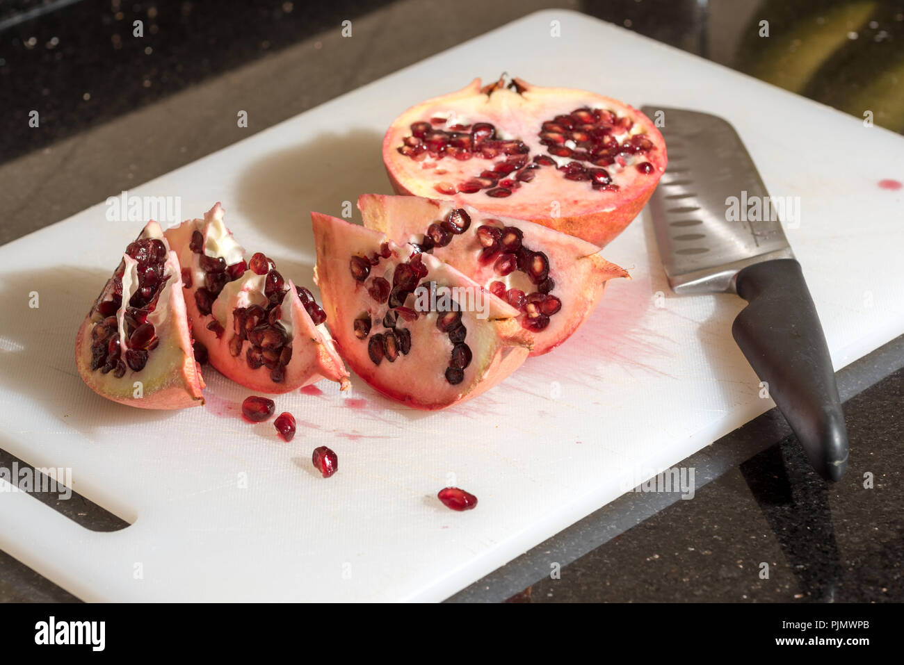 Tagliare il melograno isolato sul tagliere con coltello Foto Stock