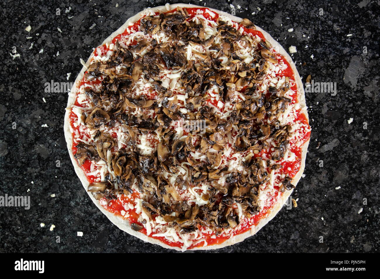 Pizza con funghi sulla tavola nera, pronto per essere messo in forno per essere cotta Foto Stock