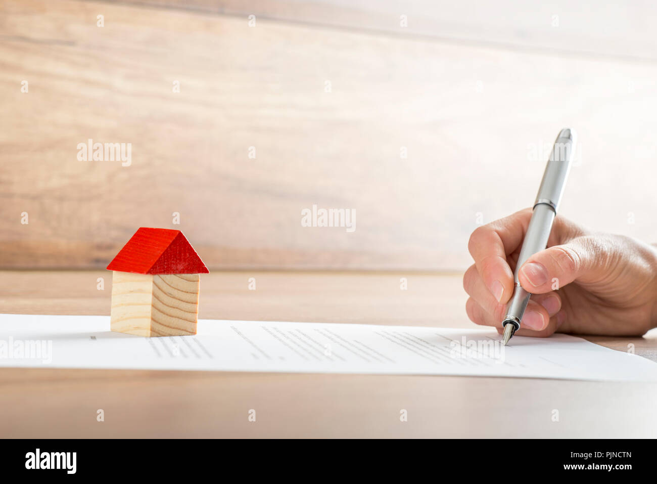 Vista dettagliata del nuovo proprietario di firmare un contratto di vendita casa ipoteca o carte con un giocattolo di legno casa sul documento. Adatto per immobili concetto Foto Stock