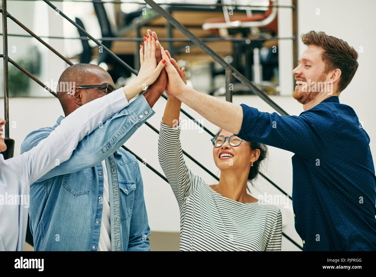 Diversi gruppi di giovani imprenditori in piedi in un ufficio moderno per celebrare il successo insieme con alta cinque Foto Stock