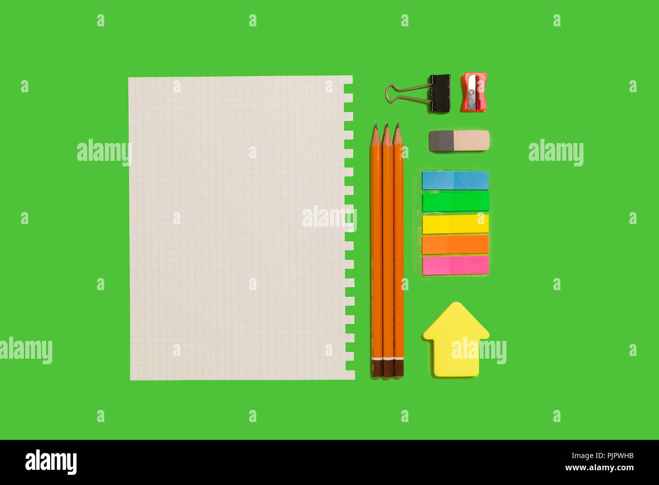 Foglio di carta bianco, matite, adesivi, gomma e un clinch giacente su di una superficie verde. concetto di cancelleria educativa. spazio libero per pubblicità tex Foto Stock