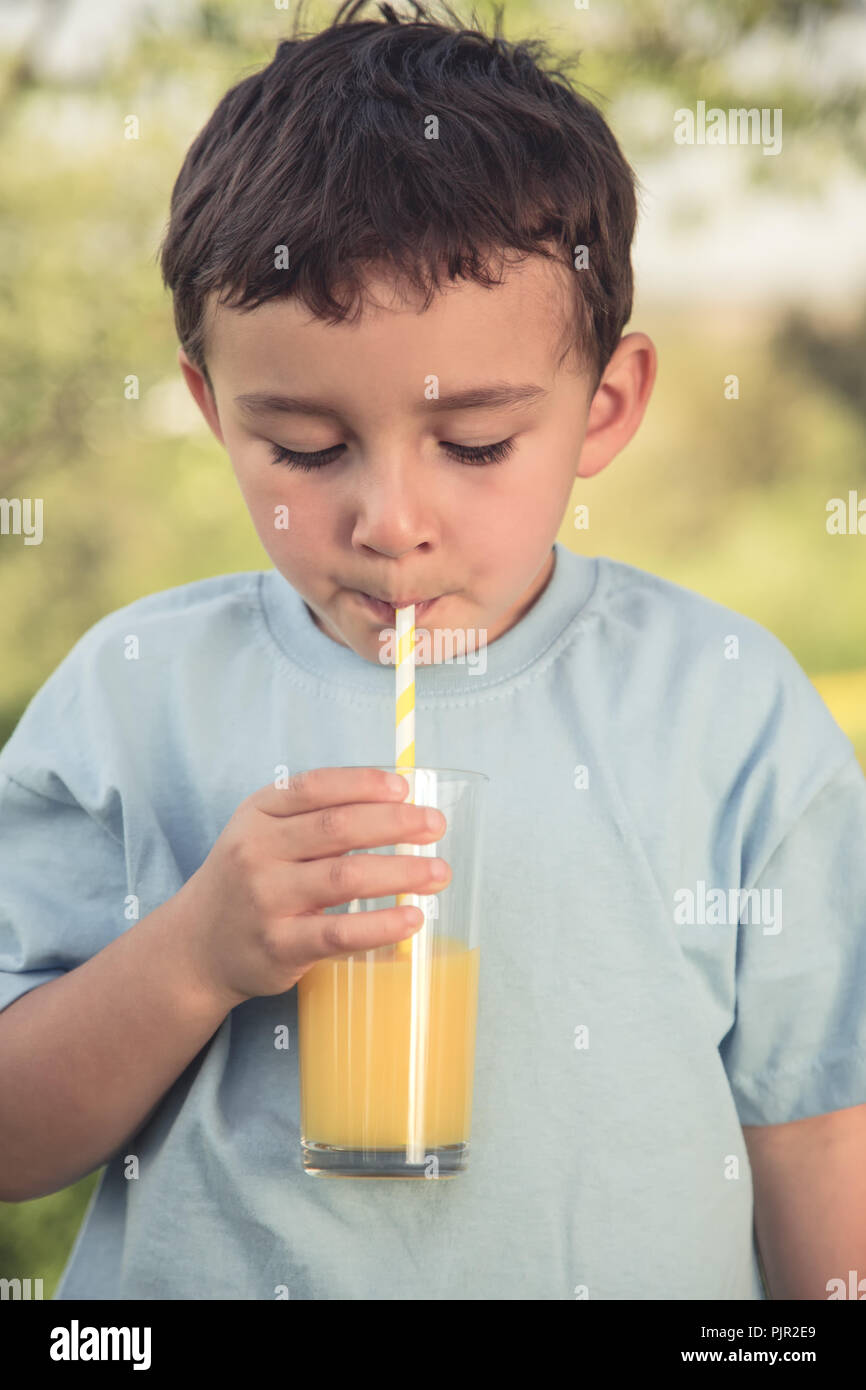 Bambino kid ragazzino di bere succo di arancia drink all'aperto look vintage formato ritratto all'aperto al di fuori del bicchiere Foto Stock