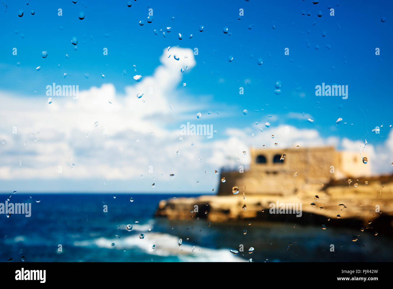 Un edificio mediterraneo a la costa visto attraverso un raindrop coperto finestra. Foto Stock