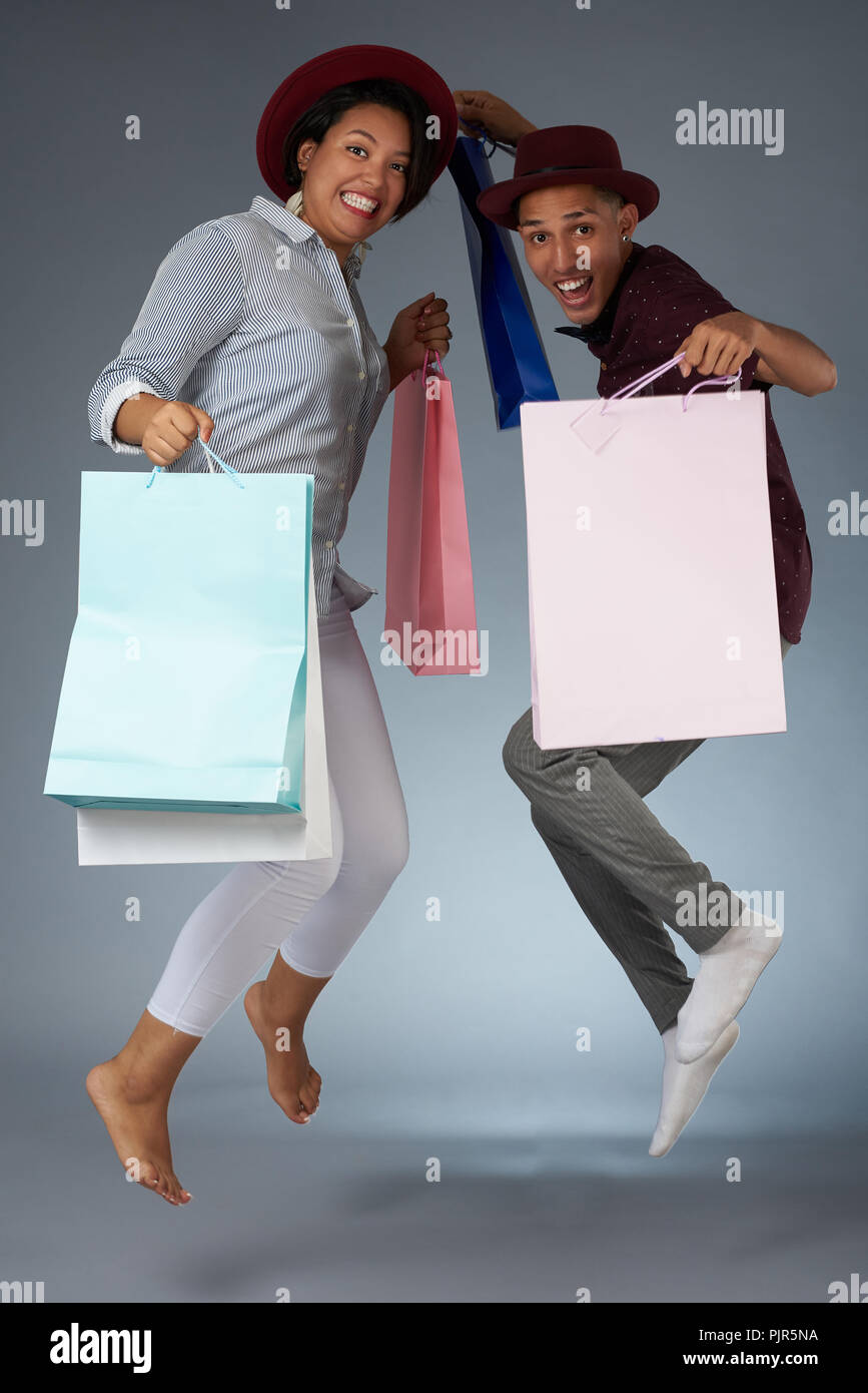 Jumping coppia giovane con le borse della spesa in isolati di sfondo per studio Foto Stock