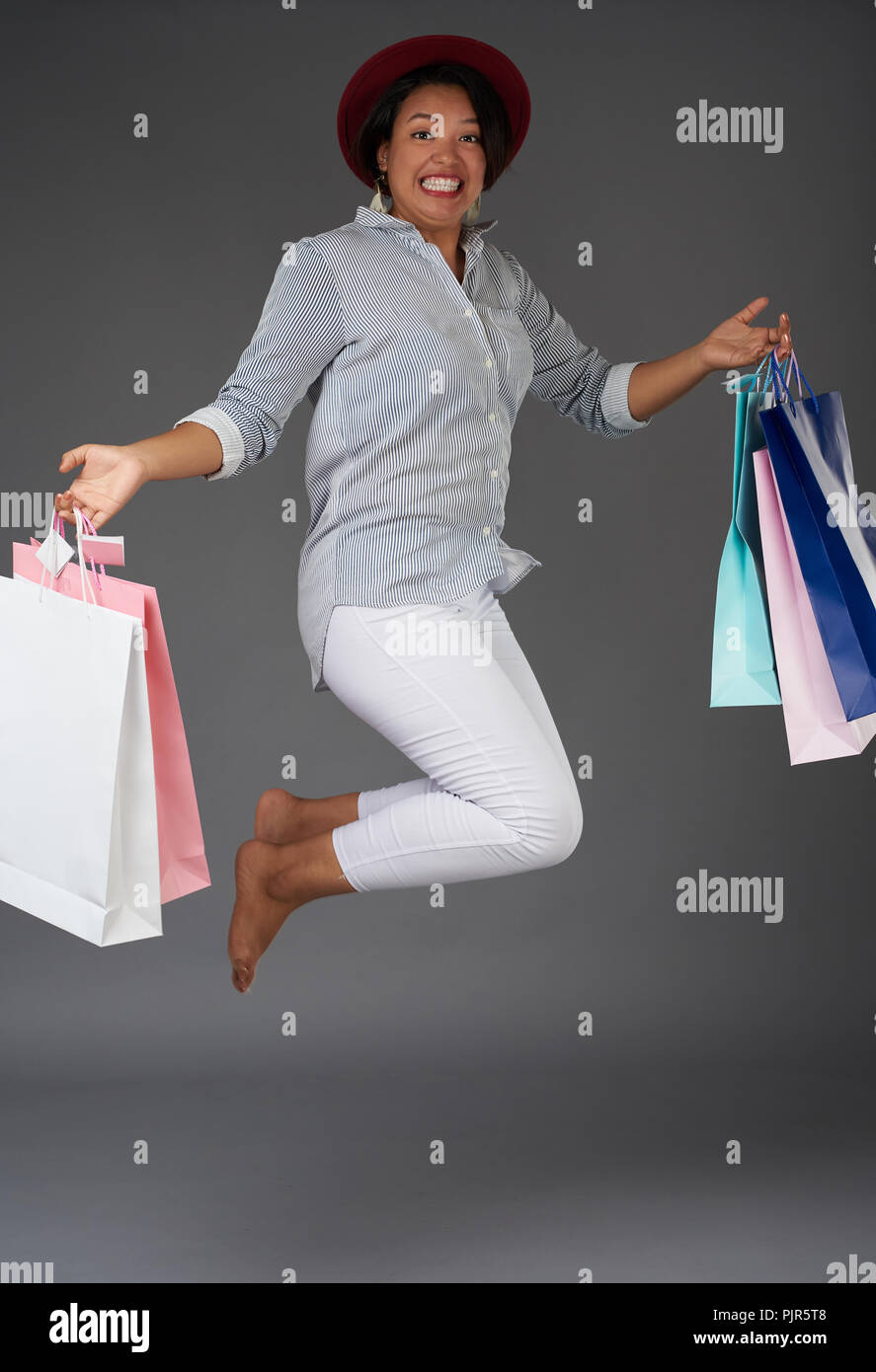 Donna jumping con coloratissime shopping bags isolato su sfondo grigio Foto Stock