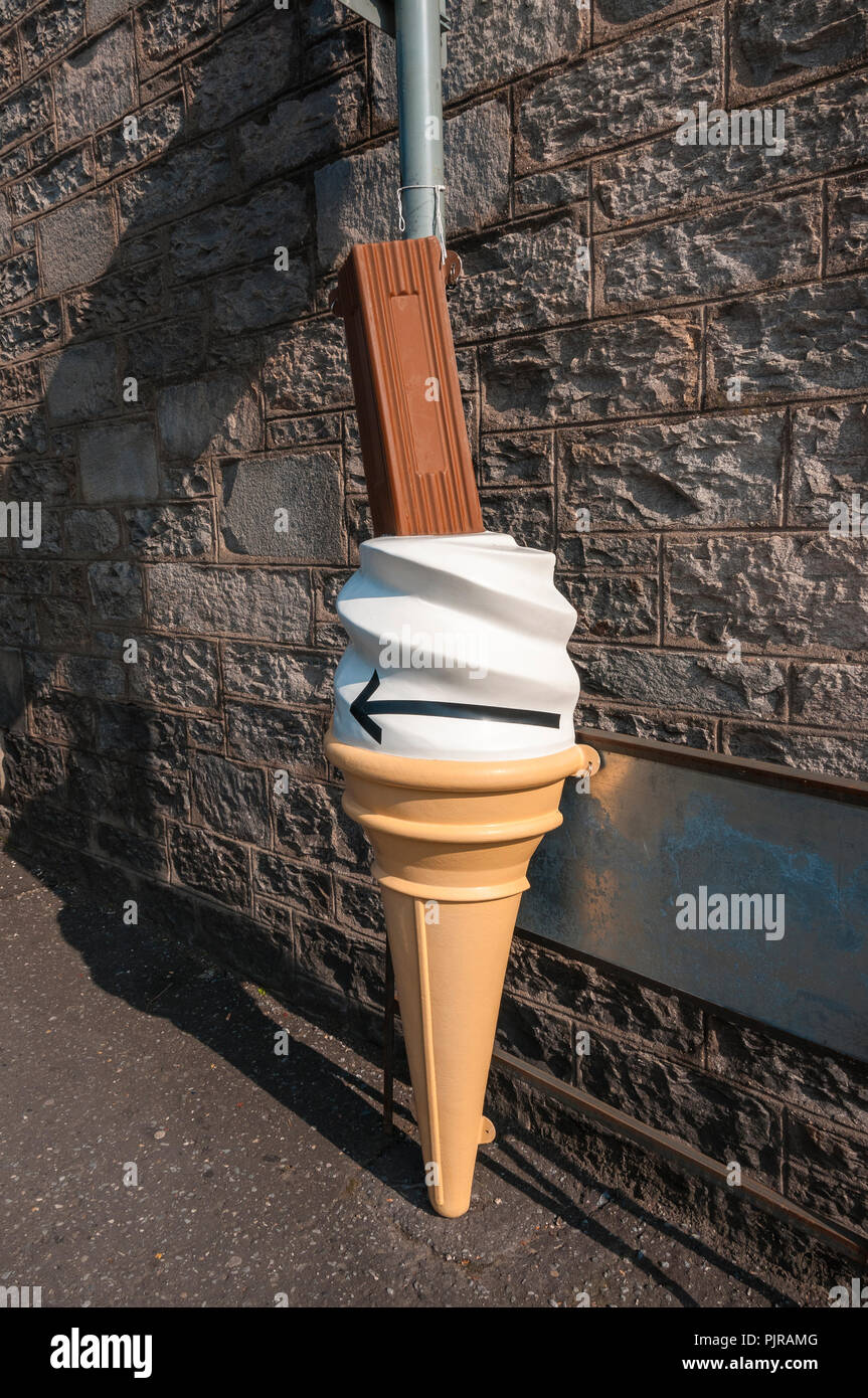 Un giudiziosamente collocati in plastica grandi ice-cream cornet con una barra di cioccolato fissato ad un cartello contro una piastra di metallo su un caratteristico muro di pietra Foto Stock