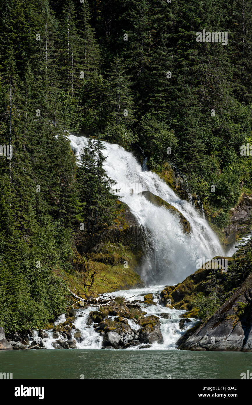 Una cascata glaciale precipita un lato montagna in lecont Bay nei pressi della lecont ghiacciaio in Isola di San Pietroburgo, Alaska. Gli iceberg calve) off Il vicino ghiacciaio LeConte che è la più meridionale la tidewater ghiacciaio dell'emisfero settentrionale. Foto Stock