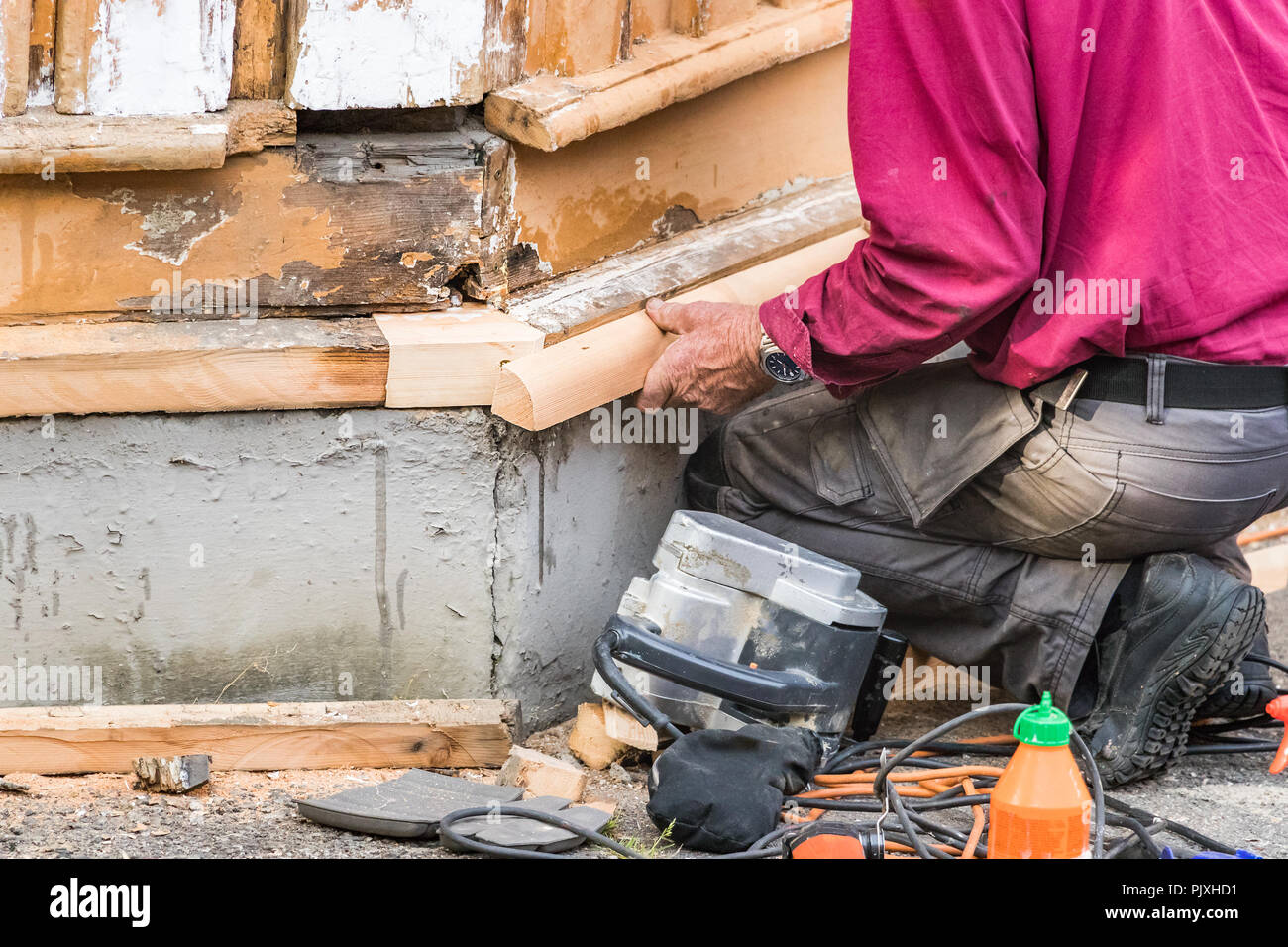 Un maschio di falegname accucciato giù il montaggio di un pezzo di legno sull'angolo di una vecchia casa in legno in Norvegia. Foto Stock