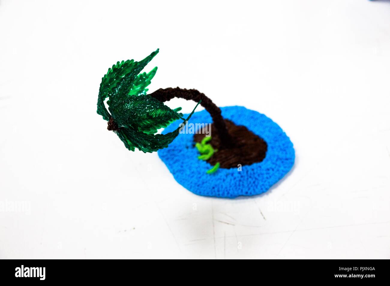 Un piccolo verde Palm tree sorge su uno sfondo bianco, inclinando il tronco. Il palmo è realizzato in plastica e dà una sensazione di calore e di una buona vacanza. Foto Stock