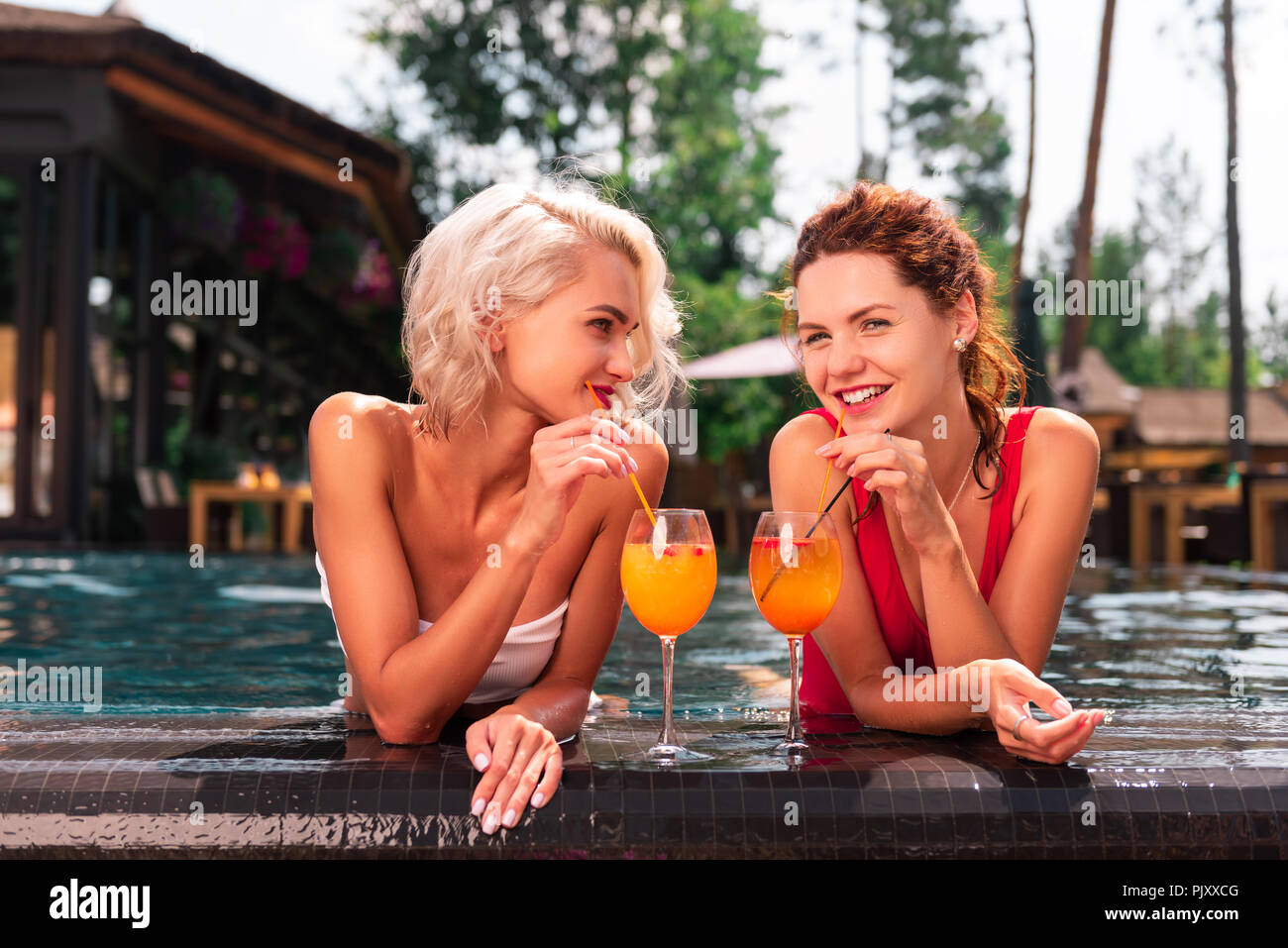 Felice di giovani donne a bere gustosi cocktail in piscina Foto Stock