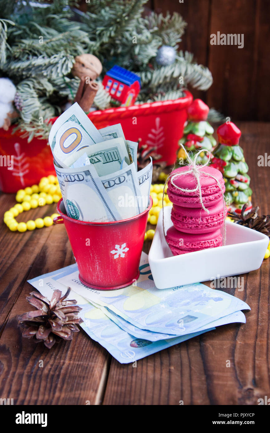 Twisted banconote di dollari ed euro in rosso il natale benna, euro e amaretti rosa. Nuovo anno di doni Foto Stock