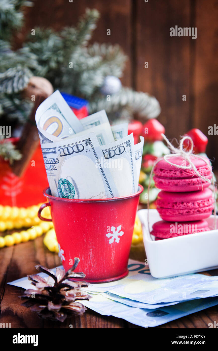 Twisted banconote di dollari ed euro in rosso il natale benna, euro e amaretti rosa. Nuovo anno di doni Foto Stock