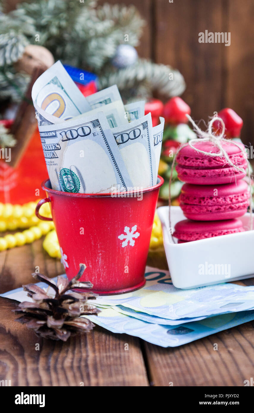 Twisted banconote di dollari in rosso la benna di natale, euro e amaretti rosa. Nuovo anno di doni Foto Stock