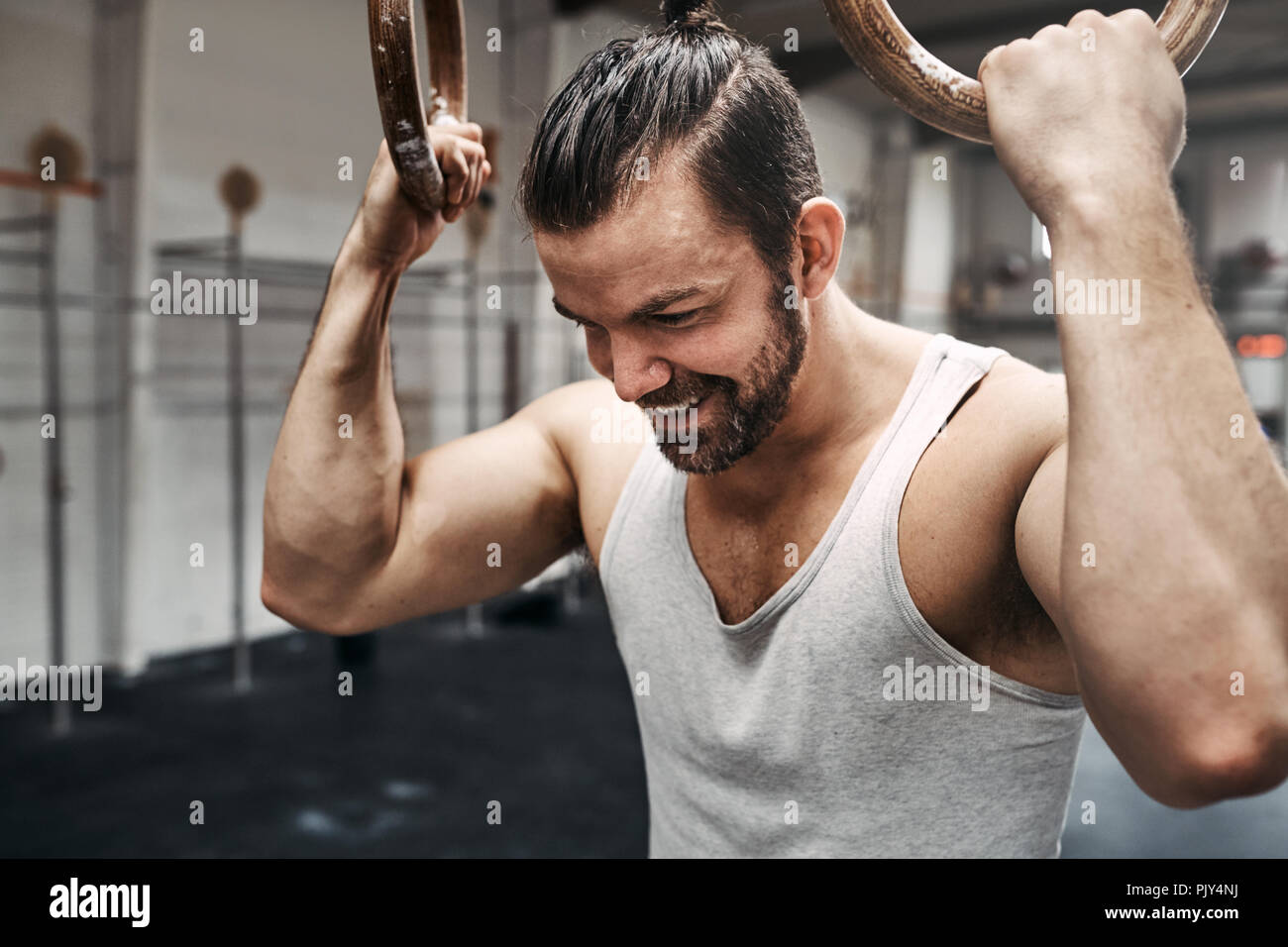 Montare il giovane uomo in abbigliamento sportivo a sorridere mentre si lavora fino a sudare durante una sessione di allenamento con anelli in palestra Foto Stock