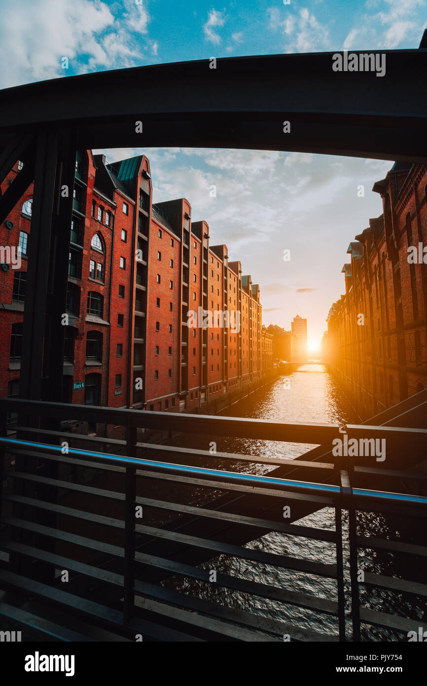 Il Red Brick Warehouse - quartiere Speicherstadt di Amburgo Germania, incorniciato da ponte in acciaio travi ad arco con vista sul canale riempito dalla calda luce del tramonto Foto Stock