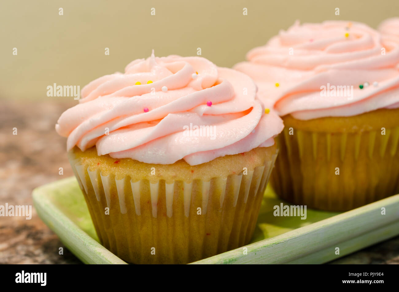 Luce rosa di crema di burro la glassa roteato sulla sommità di freschi fatti in casa tortina. Caramelle colorate spruzza spruzzata sulla parte superiore. Delizioso dolce delizia per parte. Foto Stock