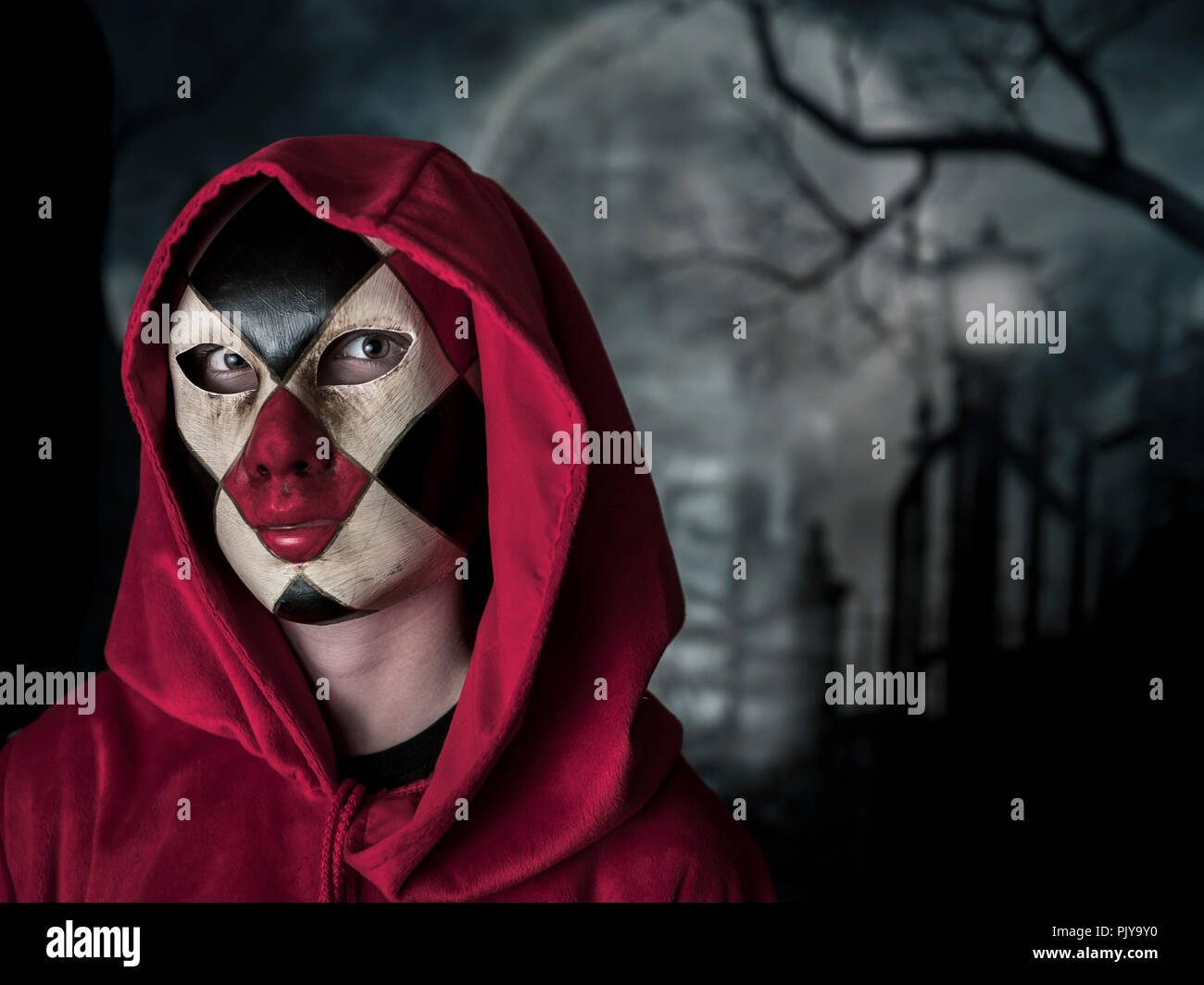 Donna mascherata indossando un nero e rosso controllato maschera veneziana nella notte con la luna piena in prossimità di un cimitero Foto Stock