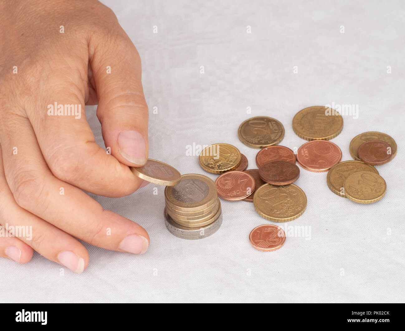Matura, donna mettendo mano monete in una pila, heap, sulla tovaglia bianca dello sfondo. Chiudere. Europeo di conio di monete metalliche in euro, conteggio spiccioli, piccolo cambiamento. Foto Stock