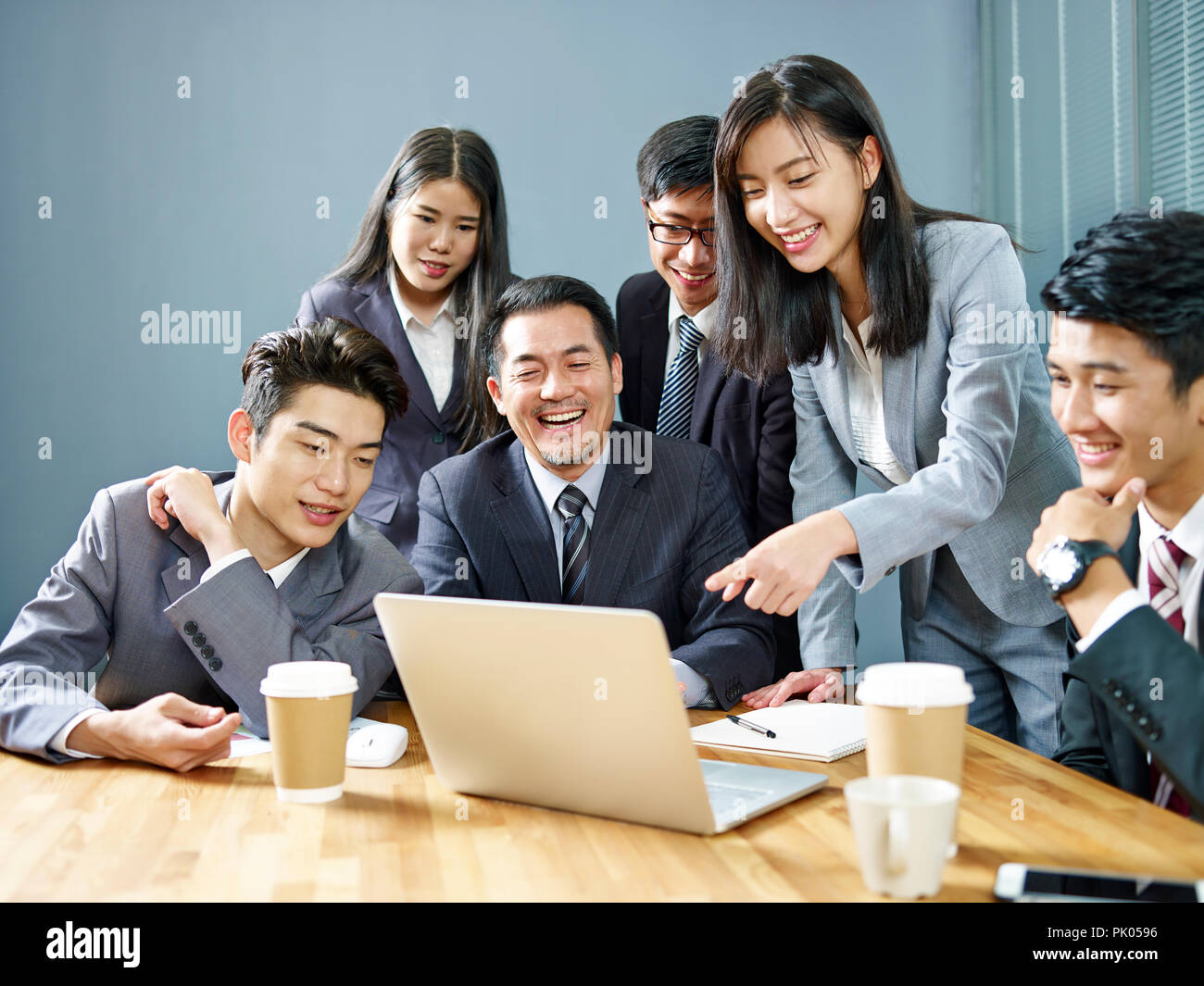 Un team di asian business dirigenti che lavorano insieme in ufficio utilizzando il computer portatile, felice e sorridente. Foto Stock