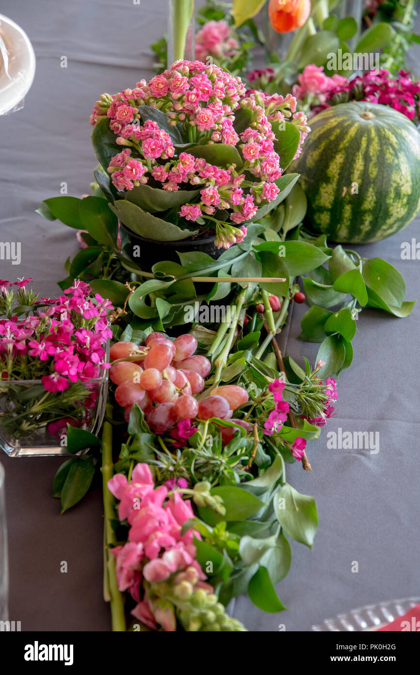 Un allestimento floreale di bellissimi fiori arancione con colorati di rosa mazzetto in primo piano con un invitante round anguria e uva. Bellissimo set di partito Foto Stock