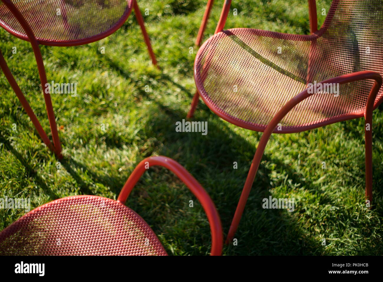 Rosso parco di metallo sedie closeup, contro l'erba verde, con ombre Foto Stock