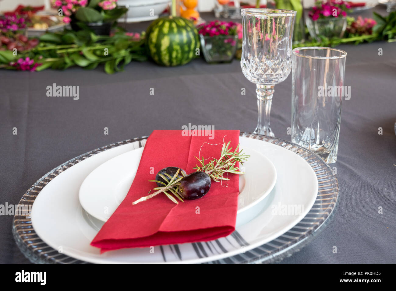 Un tavolo pranzo insieme con sotto le piastre, grazioso grigio e le piastre bianche, rosso salvietta, decorativo piccolo ramo di albero,due uve con motivi floreali e di frutta decor. Foto Stock