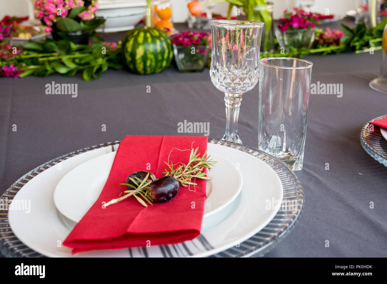 Un tavolo pranzo insieme con sotto le piastre, grazioso grigio e le piastre bianche, rosso salvietta, decorativo piccolo ramo di albero,due uve con motivi floreali e di frutta decor. Foto Stock