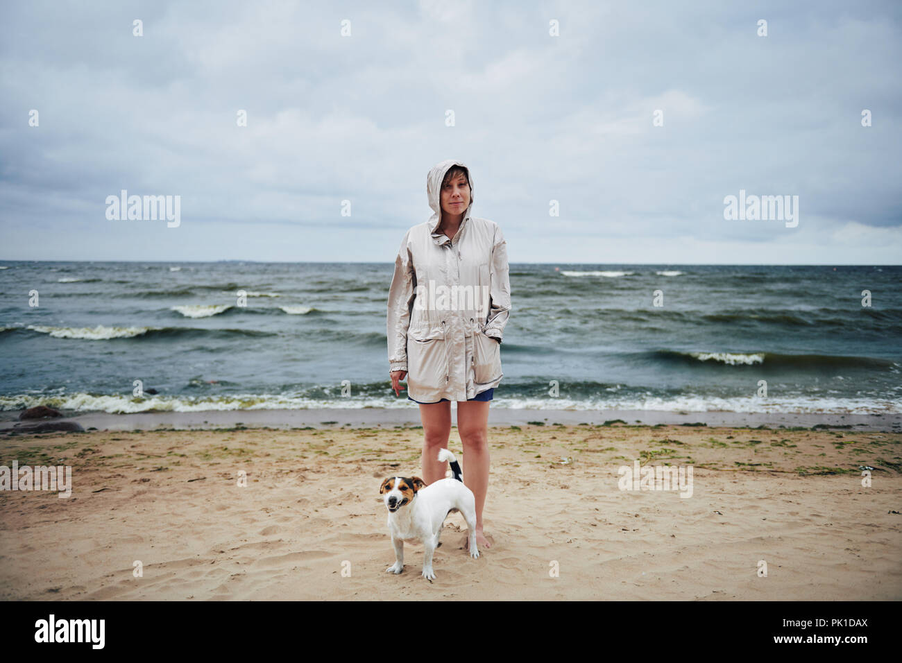 Donna in camicia guardando il cane vicino al mare Foto Stock