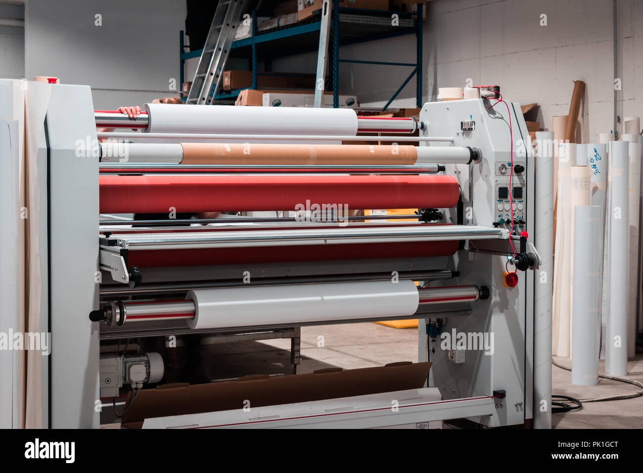 Grande stampa professionale laminatore, armati con rossi grandi rotoli di carta lucida e piccoli tubi di pellicola trasparente. Foto Stock