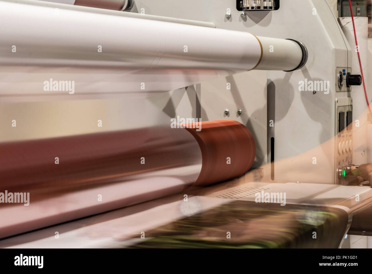 Grande stampa professionale laminatore, armati con rossi grandi rotoli di carta lucida e piccoli tubi di pellicola trasparente. Foto Stock