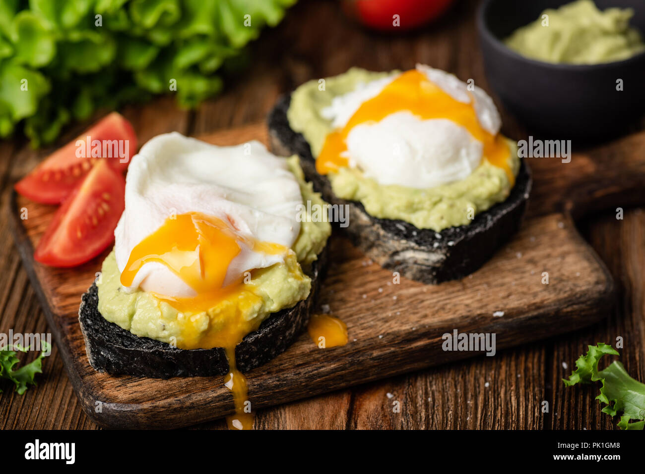 Avocado e Uovo affogato su tostati pane di carbone su una tavola di legno che serve board. Primo piano. Gustosi snack, pranzo e il cibo a colazione Foto Stock