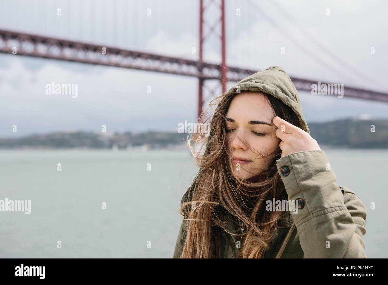 Ritratto di una giovane ragazza attraente che raddrizza i suoi capelli in tempo ventoso al di fuori di Lisbona. Foto Stock