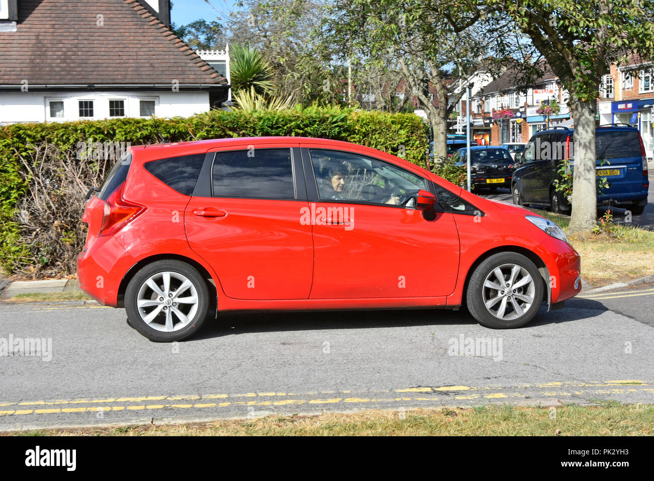 Donna anziana matura auto conducente vista laterale guida cinque porte rosso Nissan Note berlina tinta lunotto vetro in una posizione urbana Essex Inghilterra UK Foto Stock