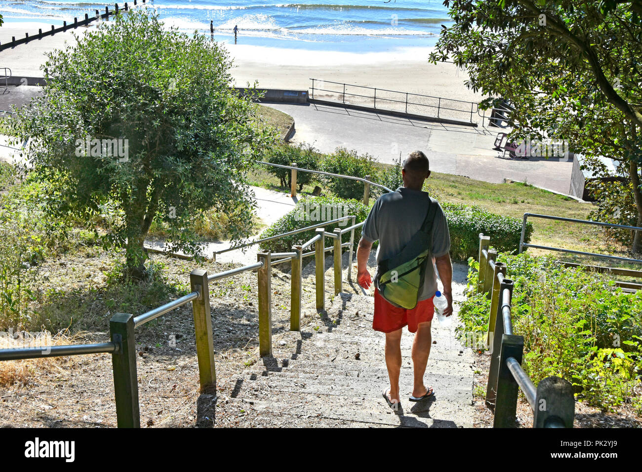 Vista posteriore dell'uomo in pantaloncini rossi a piedi verso il basso passi verso la mattina presto la gente sulla famiglia di sabbia sul mare spiaggia vacanze Frinton Essex Coast Inghilterra REGNO UNITO Foto Stock