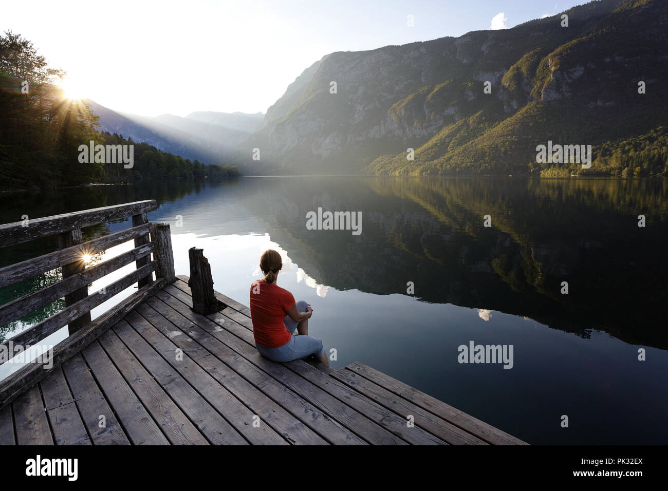 Donna seduta su un molo in legno e guardare il tramonto sopra le montagne, il lago di Bohinj, Slovenia. Foto Stock