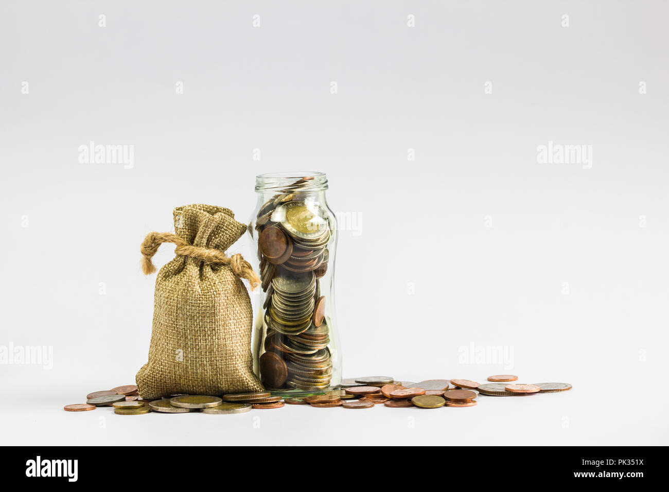 Risparmio di denaro per le future concept : Sacco sacchi, piena di monete di denaro nel vasetto di vetro e sul terreno su sfondo bianco. Foto Stock
