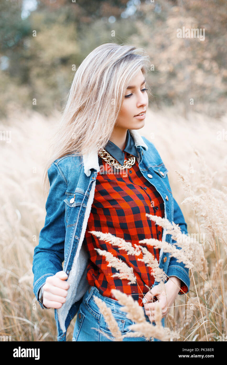 Moda elegante ragazza in un abito di denim e un rosso a scacchi camicia nel campo d'autunno con l'erba Foto Stock