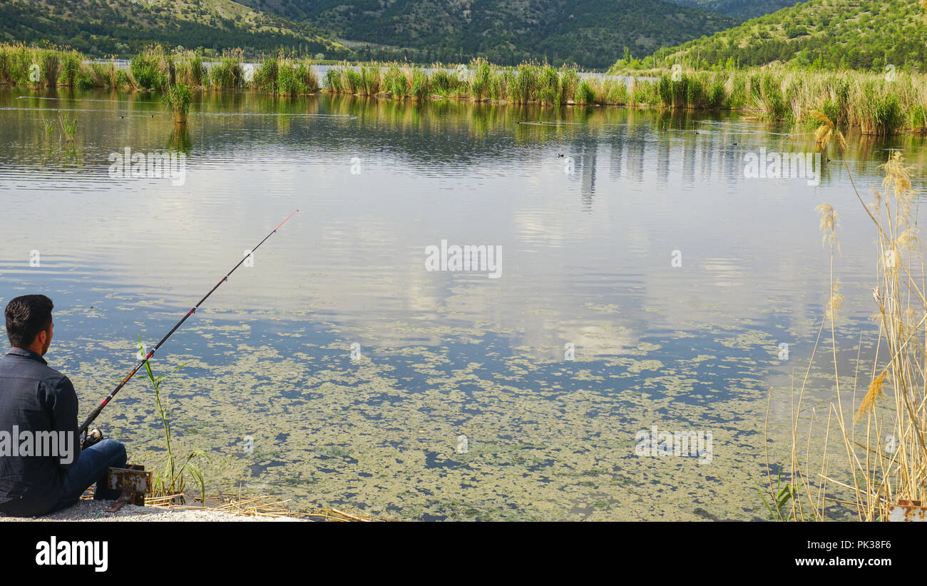 L uomo è la pesca in un lago reedy Foto Stock