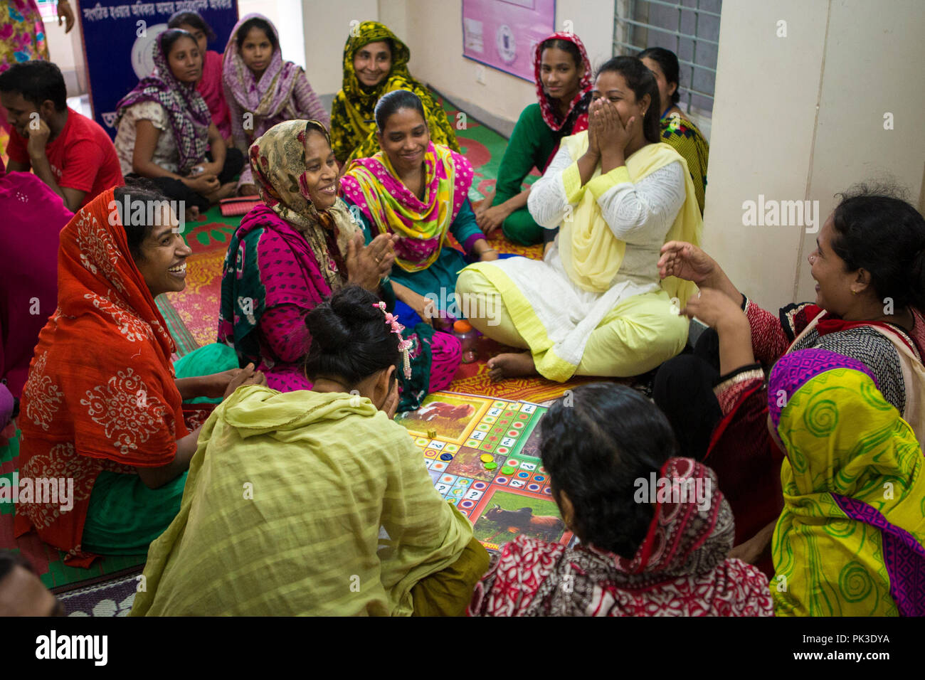 Indumento i lavoratori a ridere come essi giocare un gioco di bordo durante un workshop che si terrà a Dacca in Bangladesh. Foto Stock