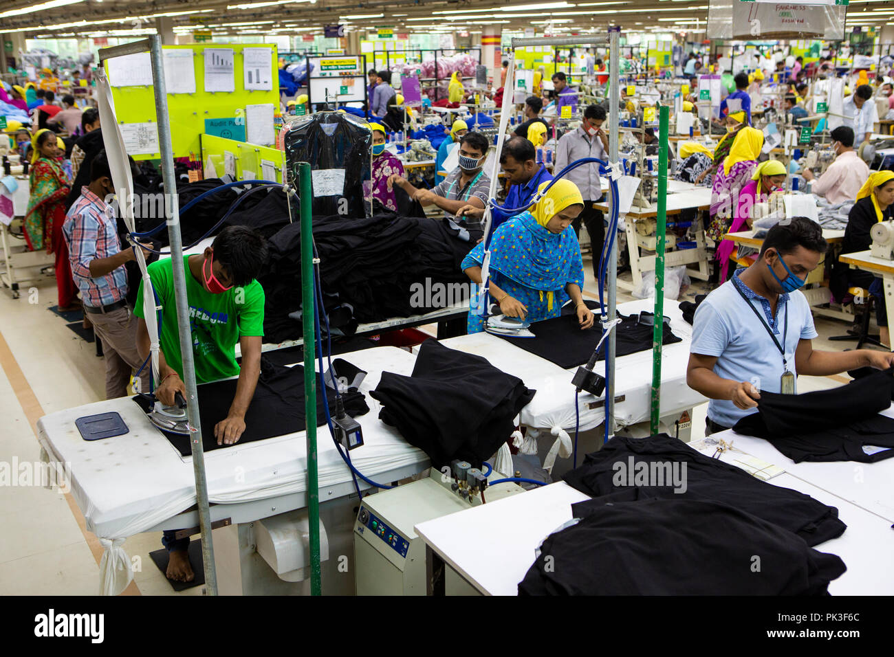Lavoratori di indumento per la stiratura e la cucitura all'interno di una fabbrica di indumento in Bangladesh. Foto Stock