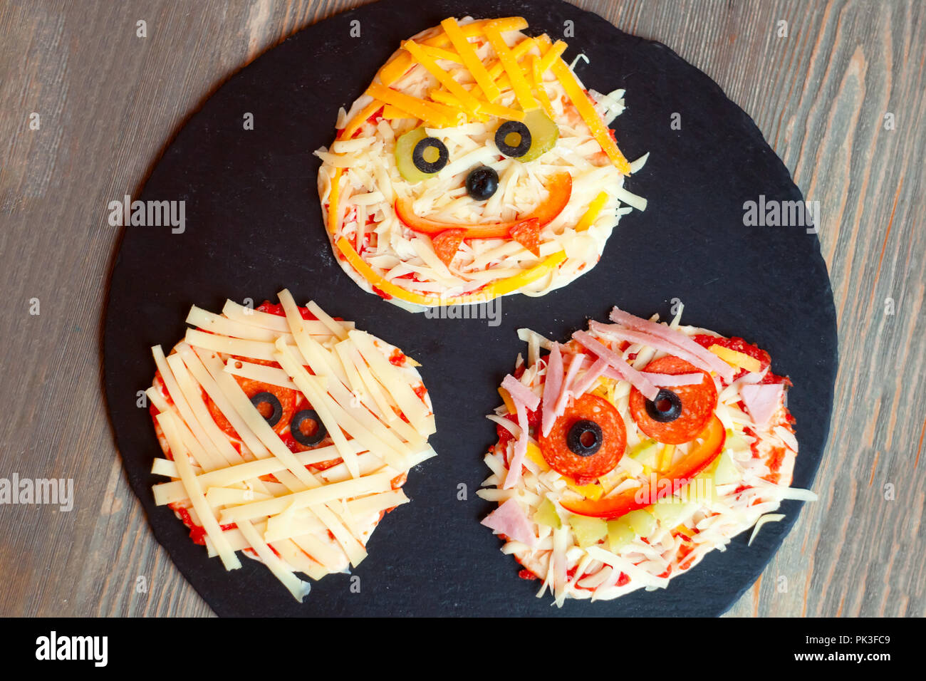 Raw pizza Halloween con mostri, al di sopra della scena con decor e su una piastra nera a prepararsi per cotto al forno, idea per la casa parte cibo, facile, sana e deliziosa fu Foto Stock