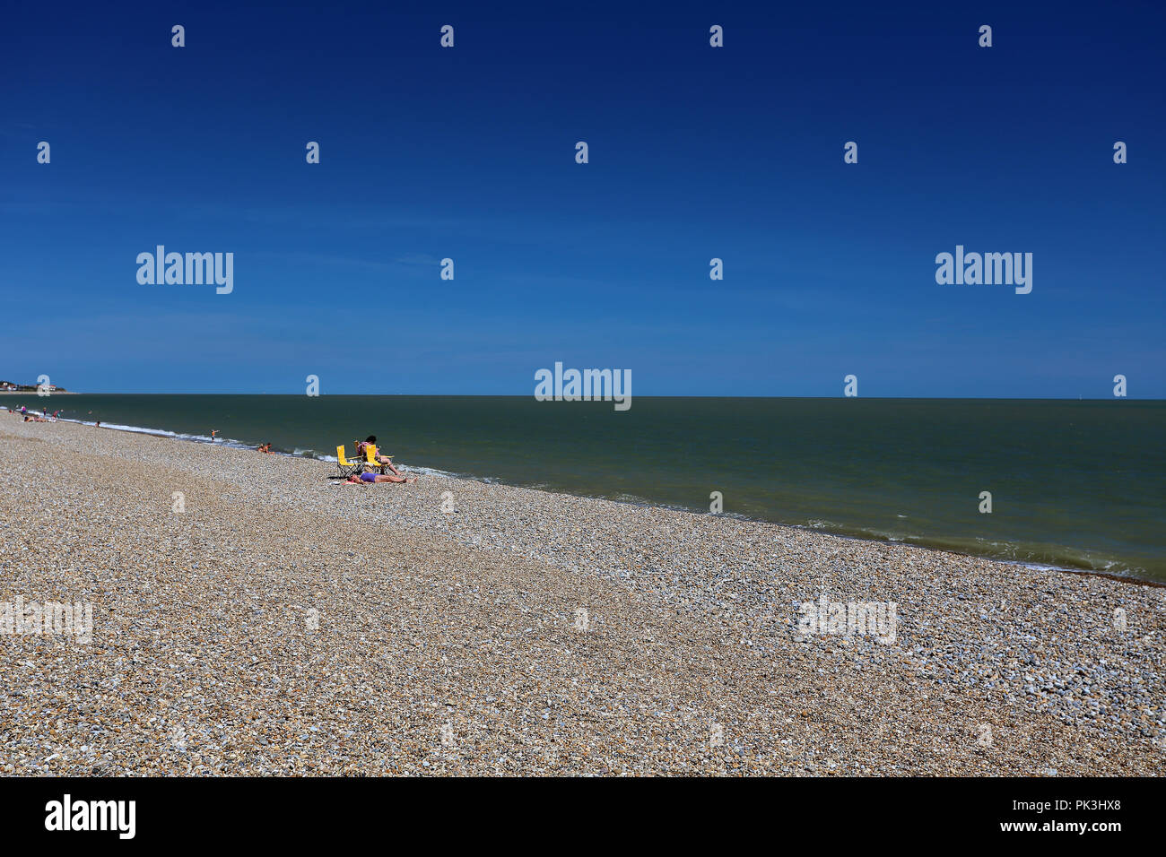 Prendere il sole vacanzieri rilassarsi in una calda giornata estiva presso la spiaggia di ciottoli a Aldeburgh, Suffolk, Regno Unito Foto Stock