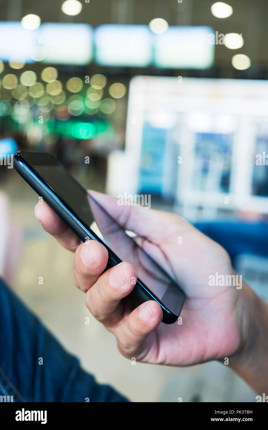 Primo piano di un giovane uomo caucasico utilizzando uno smartphone presso la sala di attesa di un treno o un autobus stazione, o un aeroporto Foto Stock