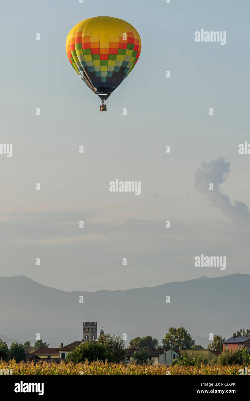Coloratissima mongolfiera vola sopra tipico villaggio nella campagna toscana nella luce del tramonto Foto Stock